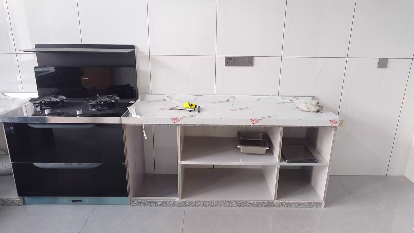 梅城李总家集成灶与不锈钢台面安装现场，台面保护膜覆盖，柜体开放格待装门板